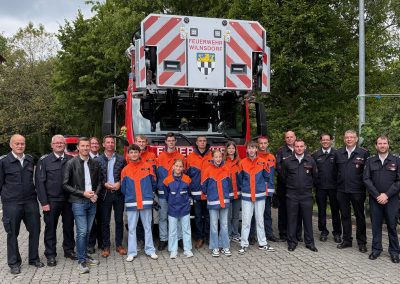 Vor einem Feuerwehrfahrzeug stehen Mitglieder der Jugendfeuerwehr Wilnsdorf, Angehörige der aktiven Wehr, die Feuerwehrleitung sowie Landrat Andreas Müller und Bürgermeister Hannes Gieseler.
