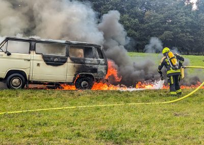 Zwei Feuerwehrleute löschen das brennende Fahrzeug mit Schaum.