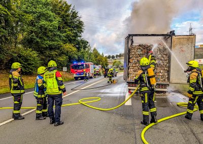 Zwei Feuerwehrmitgliede löschen den qualmenden LKW-Auflieger ab.