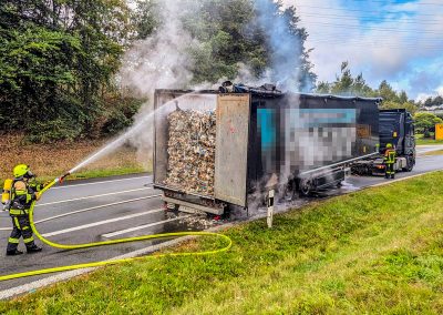 Ein Feuerwehrmitglied löscht den qualmenden LKW-Auflieger ab.