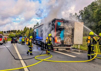 Zwei Feuerwehrmitglieder löschen den qualmenden LKW-Auflieger ab.