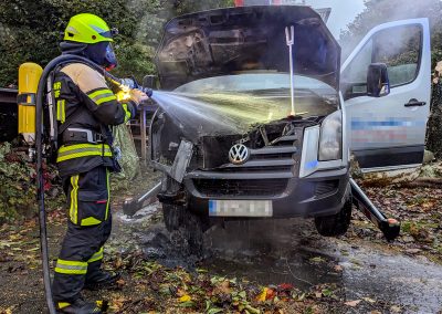 Ein Feuerwehrmitglied löscht den brennenden Motorraum mit Wasser.