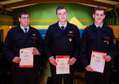 Ehrung für zehnjährige aktive Mitgliedschaft: Drei Feuerwehrleute werden ausgezeichnet und zeigen ihre Urkunden.