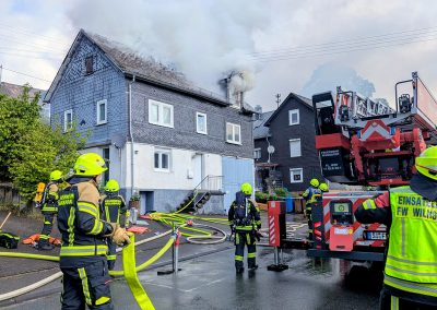Feuerwehreinsatz mit mehreren Feuerwehrleuten bei einem Wohnhausbrand mit dichter Rauchentwicklung aus dem Dachstuhl.