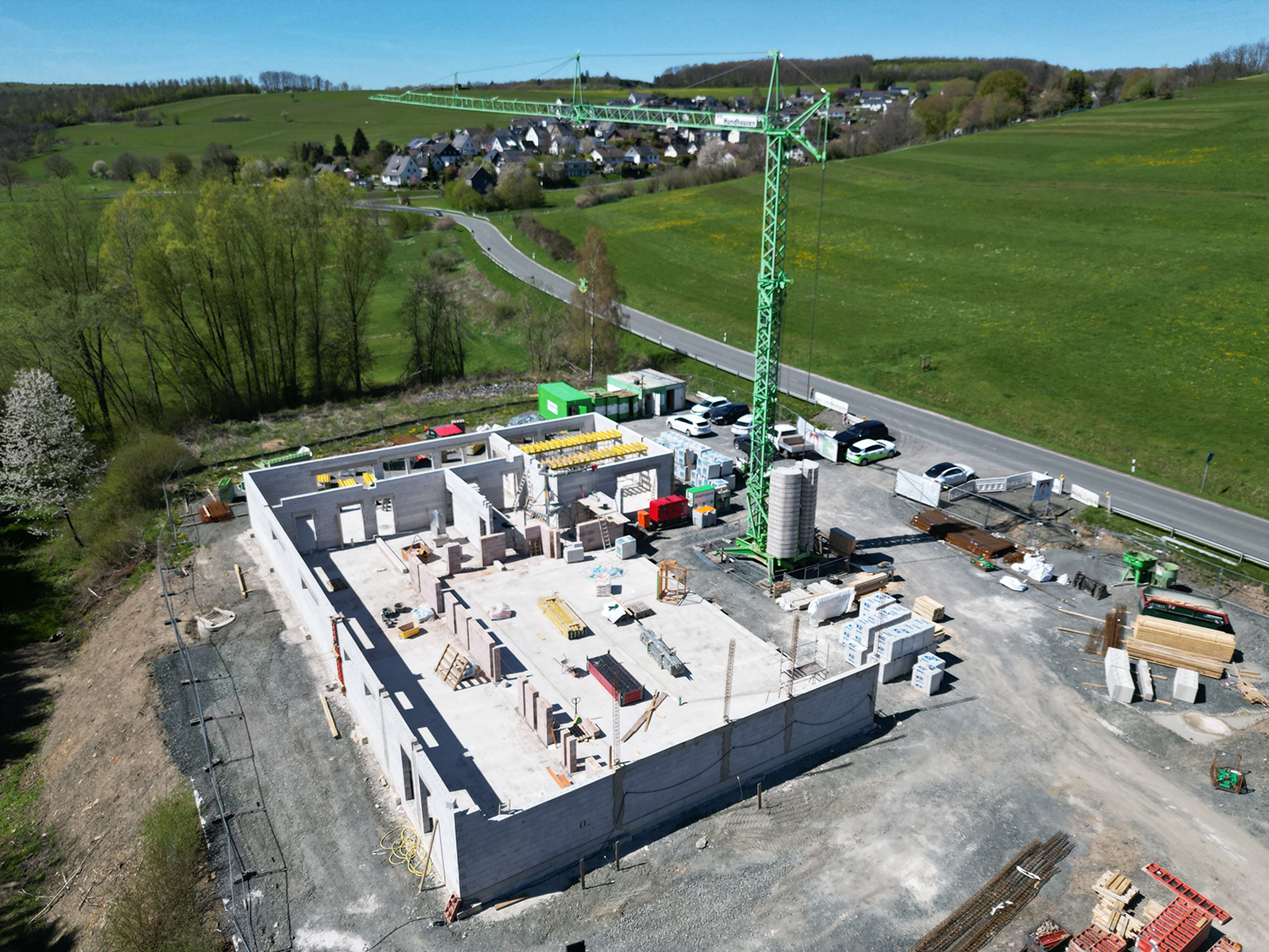 Luftaufnahme von der Baustelle für das neue Feuerwehrgerätehaus. Zu sehen sind das Fundament und die ersten Mauern des Gebäudes sowie ein großer grüner Baukran auf dem Gelände.