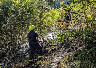 Zwei Feuerwehrkräfte bei Löscharbeiten an einem steilen Waldhang.