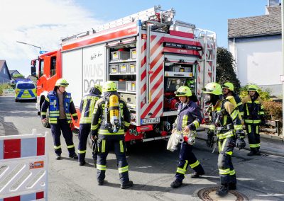 Sieben Feuerwehrleute bei einem Einsatz an einem Einsatzfahrzeug der Feuerwehr, zwei davon tragen Atemschutz.