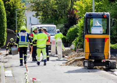 Feuerwehr und Rettungskräfte im Einsatz bei einem Gasleck an einer Baustelle mit einem gelben Minibagger.