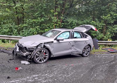 Seitenansicht eines grauen Unfallfahrzeuges mit starker Beschädigung an Front und Fahrerseite sowie ausgelösten Airbags.